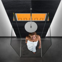 frau im weißen badetuch unter runder deckenbrause in glasdusche vor anthrazit fliesen mit orange fliesenheizmatte