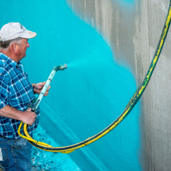 handwerker sprüht türkisfarbene spritzabdichtung auf betonwand mit spritzpistole und schlauch