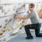handwerker kneiend befestigt isover vario km duplex uv dampfbremse mit grauem karomuster und gelben symbolen