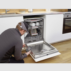 techniker mit endoskopkamera vor offenem einbaugeschirrspüler mit geschirr in weißer küche