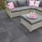 graue rattan-loungeecke mit grauen polstern pinken kissen auf großformatigen anthrazit porzellan terrassenplatten