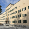 mehrstöckiges gebäude mit gelblicher fassade weiß gerahmten fenstern grünen holzläden und rampe mit metallgeländer