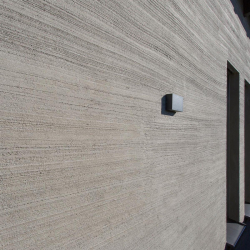 fassade mit grob strukturiertem putz in horizontalen rillen und quadratischer grauer wandleuchte