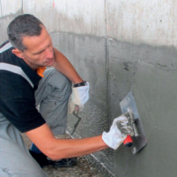 handwerker kniend glättet zementputz an wand mit...