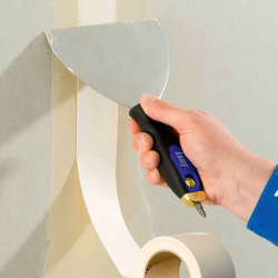 hand mit knauf multifunktions-spachtel edelstahlklinge schwarz-blauer griff beim abziehen von tapetenbahn neben papierrolle