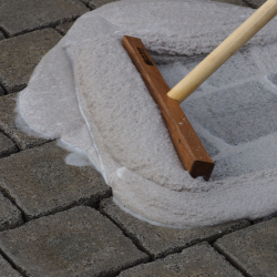 holzbesen mit langstiel verteilt hellgrauen fugensand in fugen von betonpflastersteinen